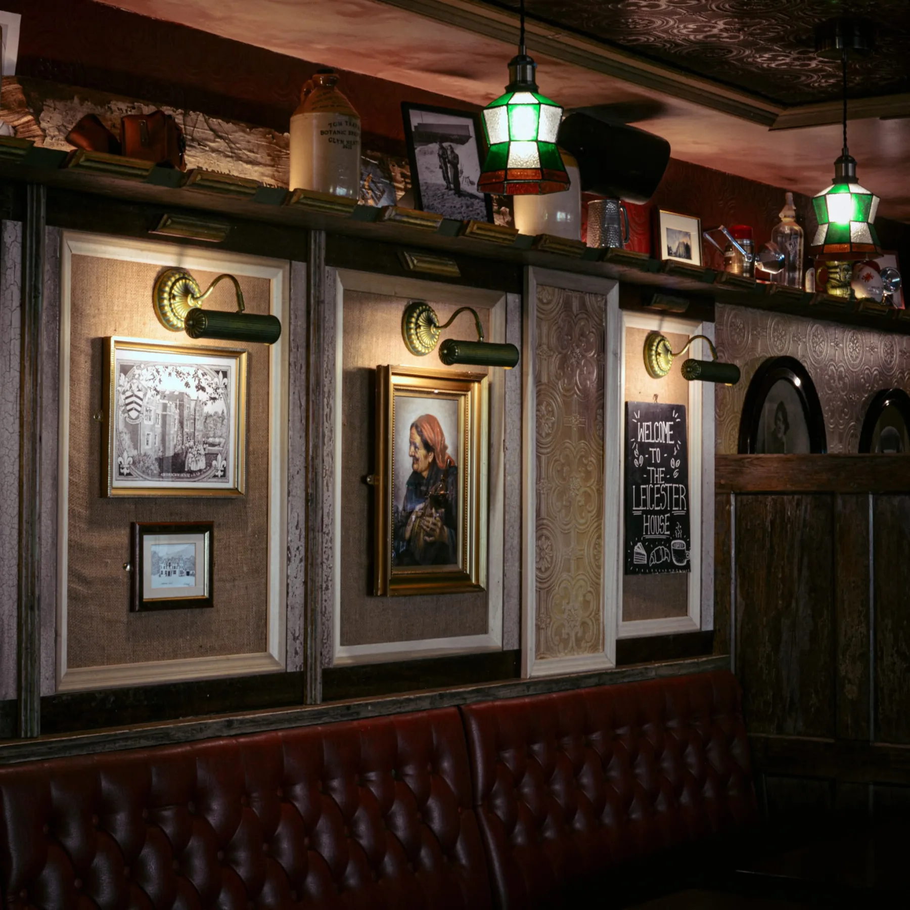 Inside Leicester House: green stained-glass pendants over the panelled wall of framed prints and the red leather banquette