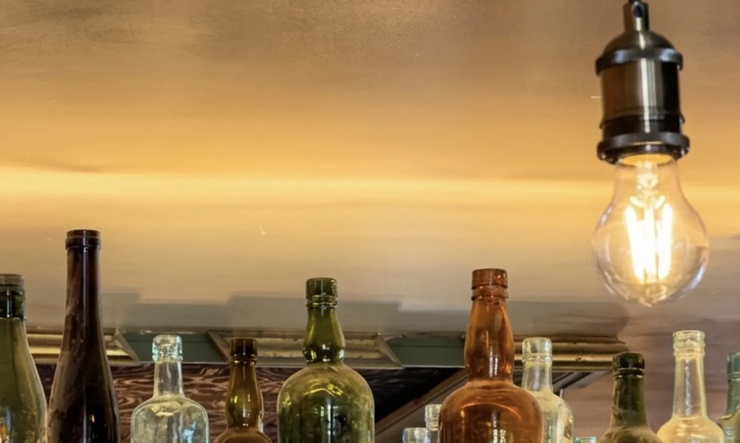 Antique bottles glowing under a filament bulb above the bar
